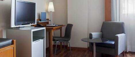 Una habitación de hotel con escritorio, una silla, televisor, lámpara y una mesita.