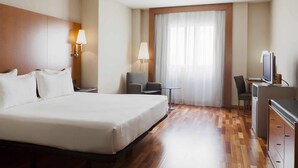 A hotel room with a large bed, two bedside lamps, a desk with a chair, a television, and a window with curtains. - Hotel Ciudad de Lleida (Lleida)