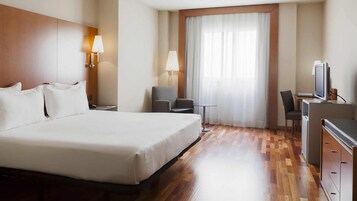 Habitación de hotel con una cama grande, dos lámparas de noche, un escritorio con una silla, un televisor y una ventana con cortinas.