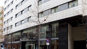A modern hotel with a glass facade, a no parking sign, and a tree in front. - Hotel Ciudad de Lleida (Lleida)