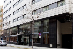 Un hotel moderno con fachada de vidrio, un letrero de no estacionamiento y un árbol en frente.