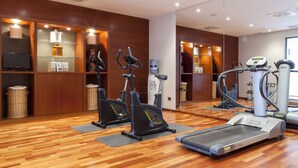 A gym with exercise equipment, wooden floors, and a mirrored wall. - Hotel Ciudad de Lleida (Lleida)