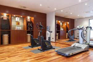 Un gimnasio con equipo de ejercicio, piso de madera y un espejo grande.
