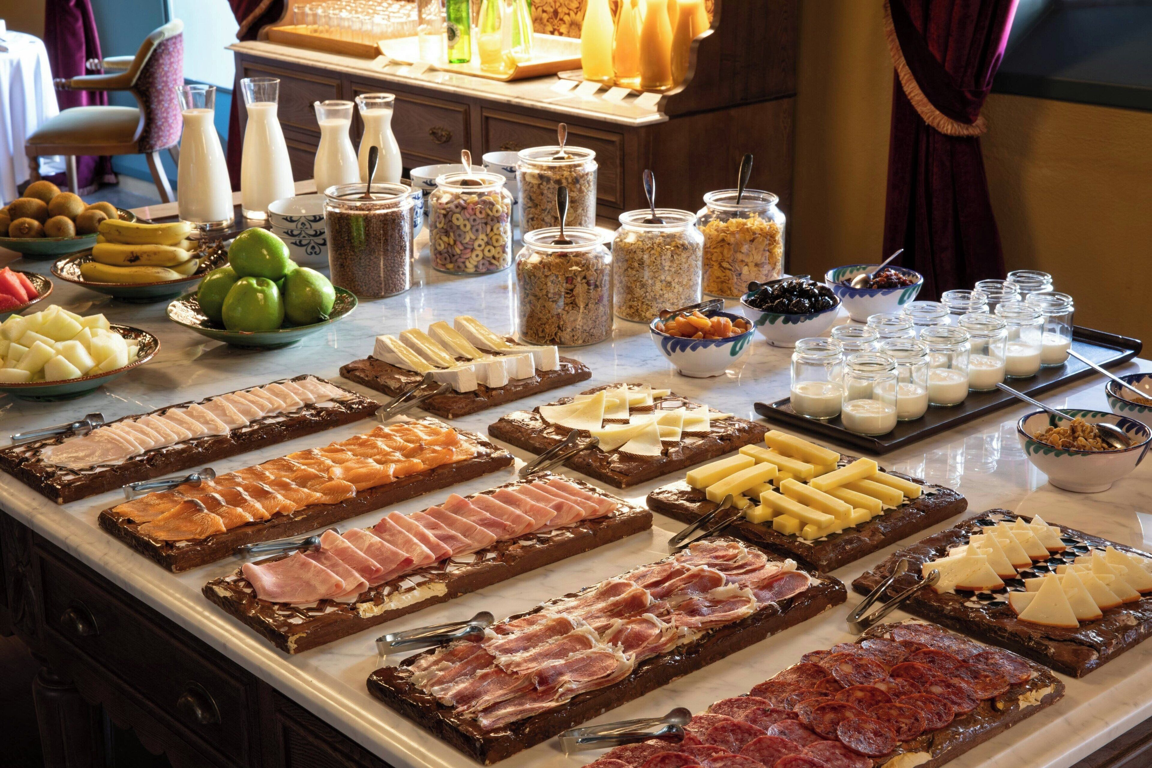 A buffet with various food items including meats, cheeses, fruits, and dairy products.