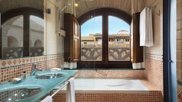 A bathroom with a glass vanity, two sinks, a bathtub, and a large arched window with a view of buildings.