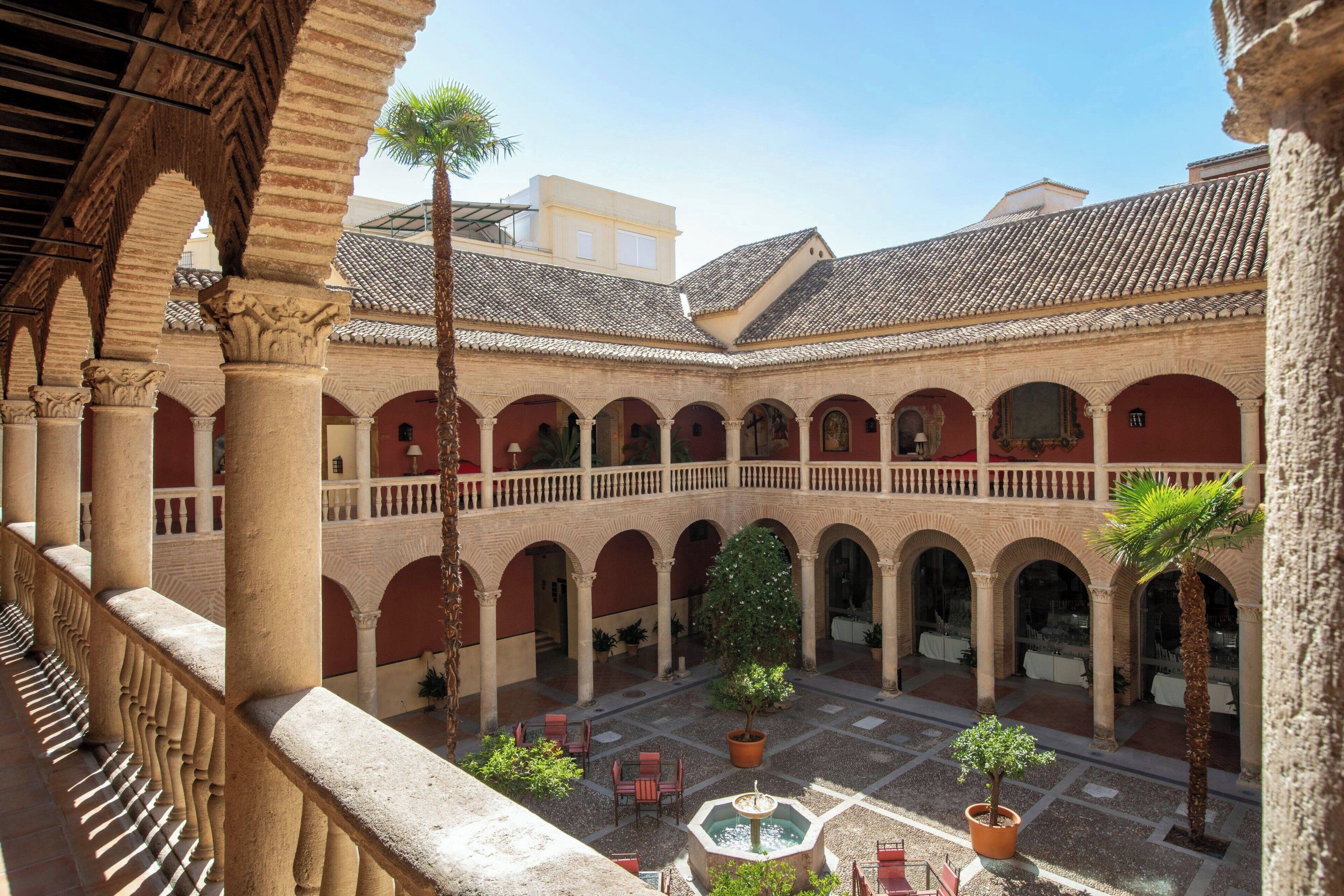 A courtyard with arches, a fountain, and potted plants.
