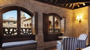 A room with a bench, two chairs, a table, and arched windows with a view of buildings outside. - Hotel Palacio de Santa Paula, Autograph Collection (Granada)