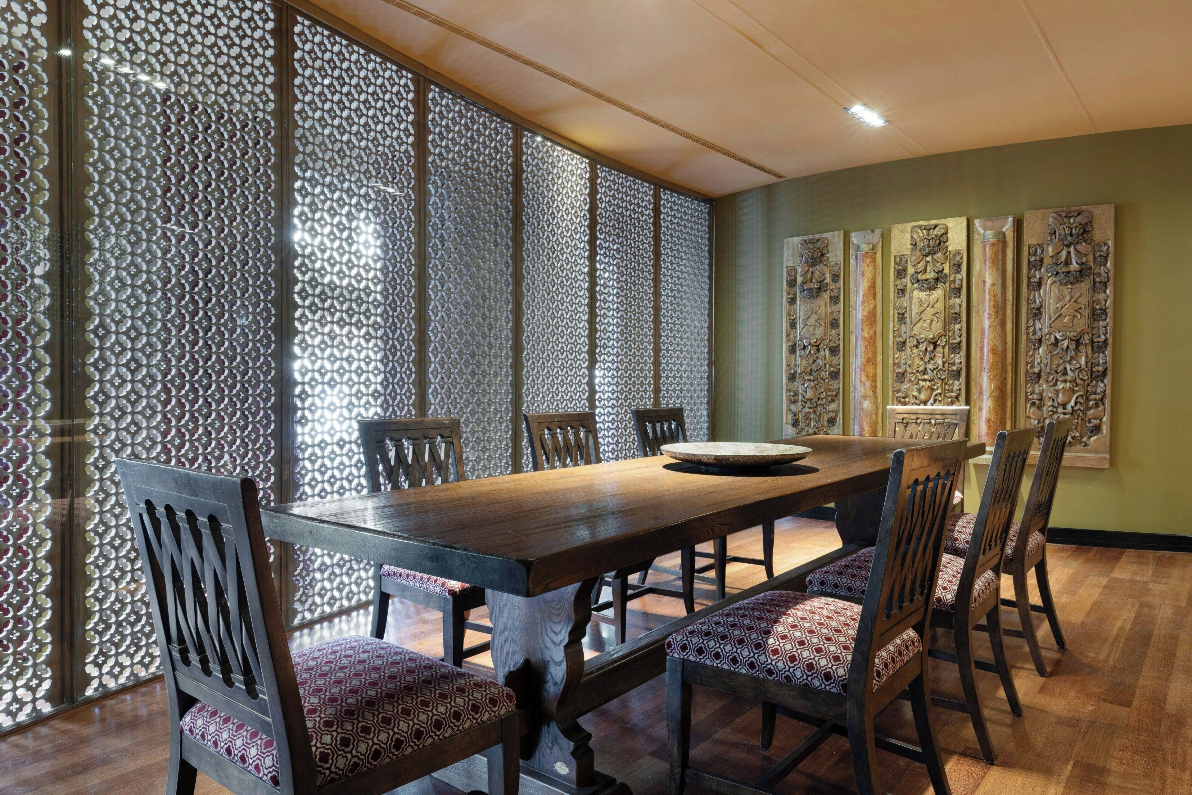 Un coin repas avec une table et des chaises en bois, un paravent décoratif et des œuvres d’art traditionnelles accrochées au mur.