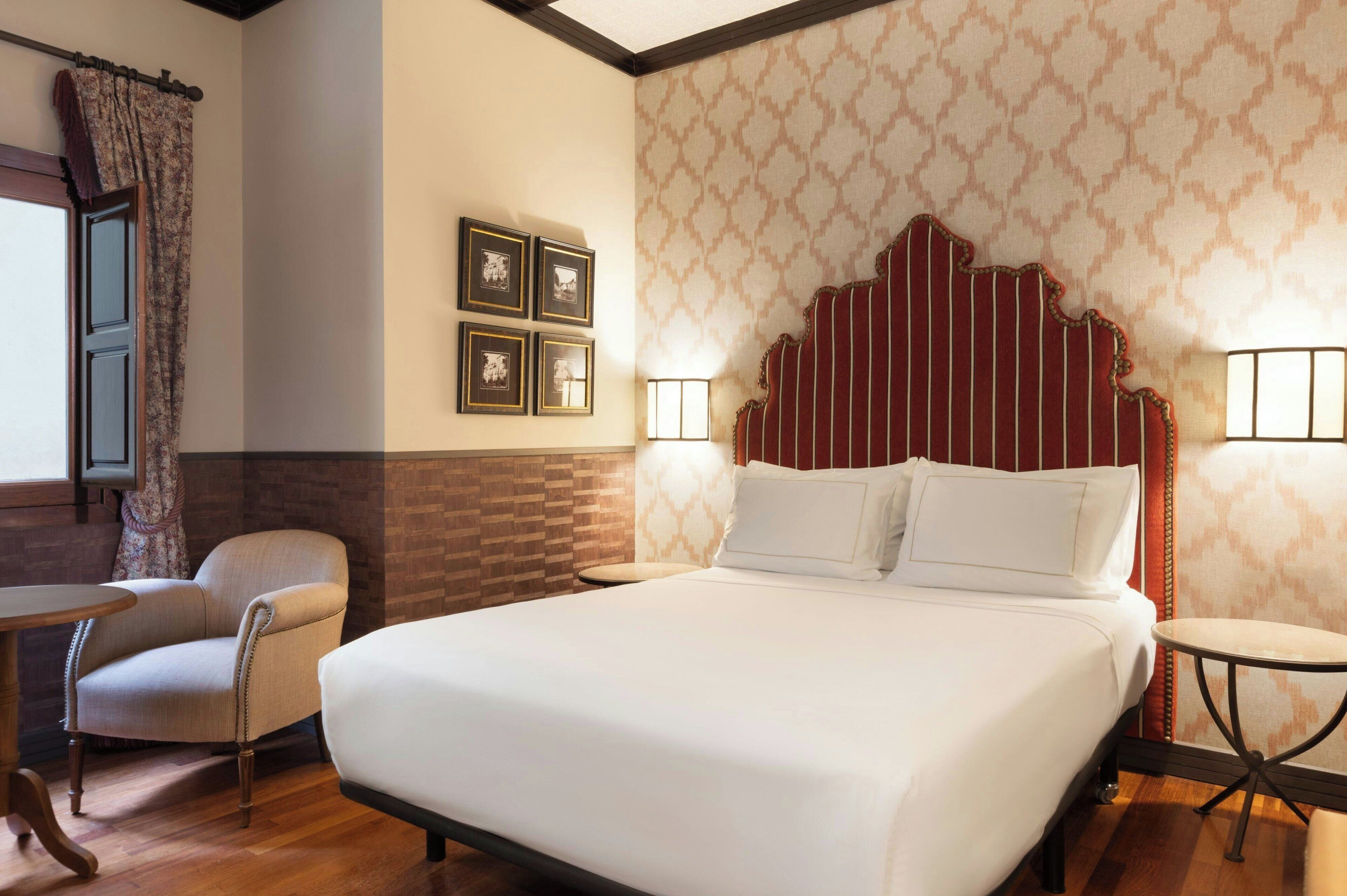 Una habitación de hotel con una cama grande, una silla, una mesita y un papel tapiz estampado.