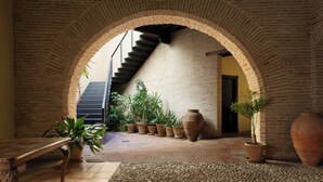 An arched brick corridor with a staircase, potted plants, and a large terracotta pot. - Hotel Palacio de Santa Paula, Autograph Collection (Granada)