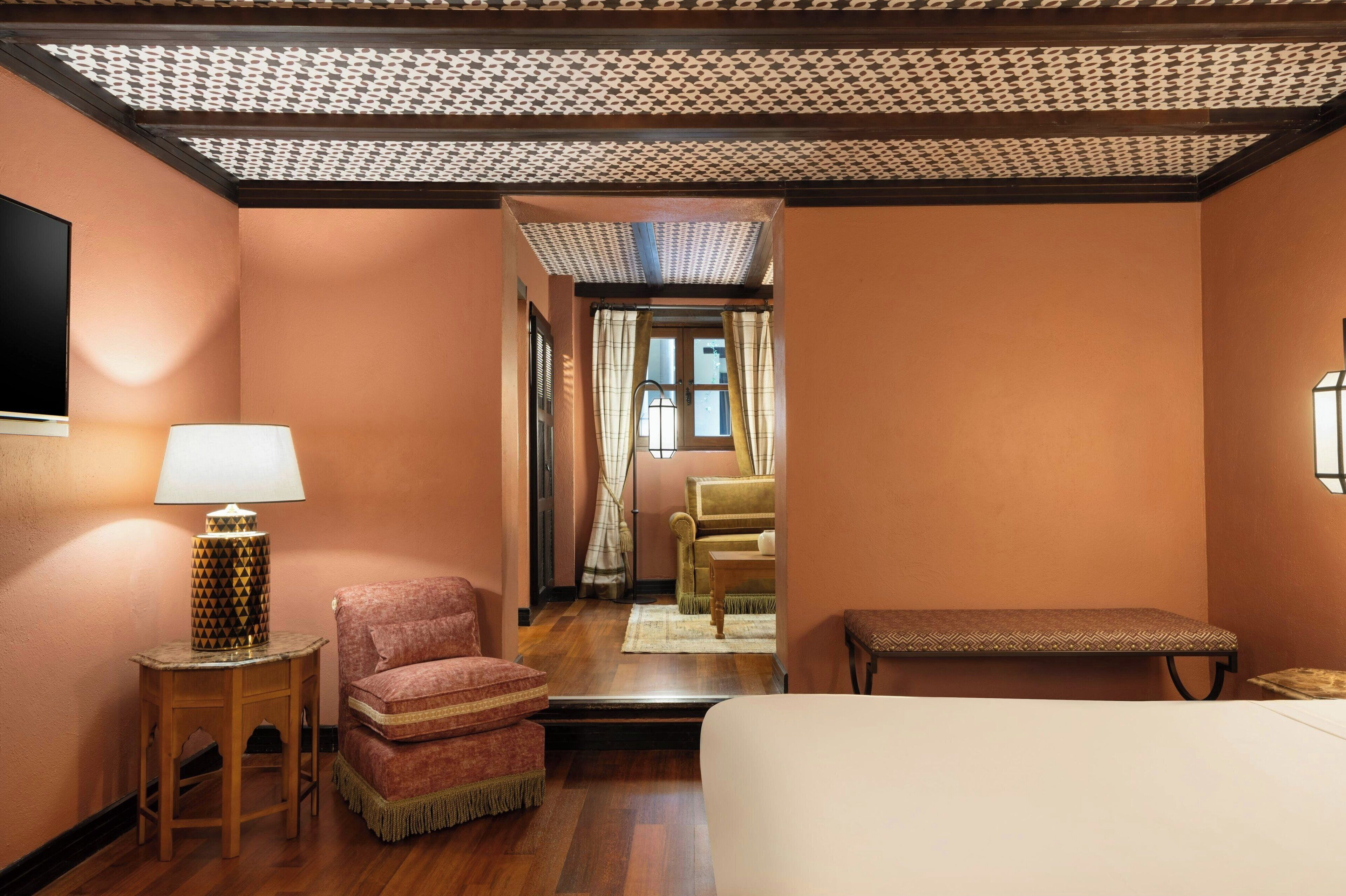Une chambre d’hôtel avec un lit, une chaise, une petite table avec une lampe et un banc.