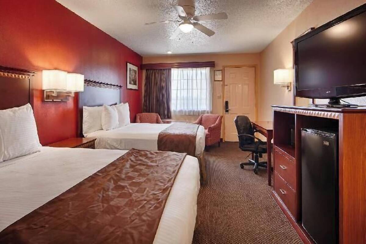Quarto de hotel com duas camas, uma escrivaninha, televisão e ventoinha de teto.
