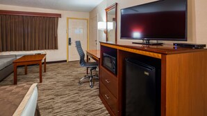 A hotel room with a flat-screen TV, a refrigerator, a desk with a chair, a sofa, and a window with curtains. - Best Western Executive Inn (Marshall)