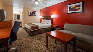 A hotel room with a bed, a desk, a chair, a sofa, a ceiling fan, and a framed picture on the wall. - Best Western Executive Inn (Marshall)