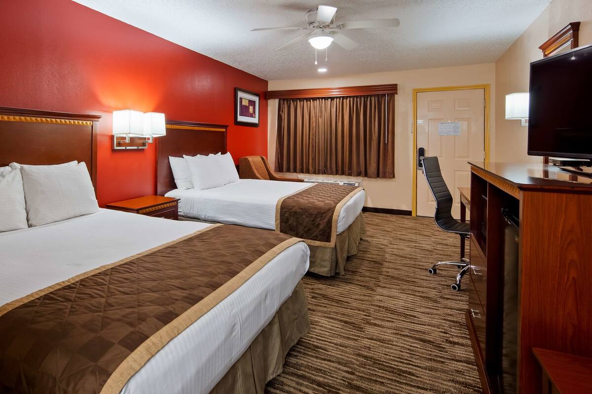Quarto de hotel com duas camas, uma escrivaninha, televisão e ventoinha no teto.