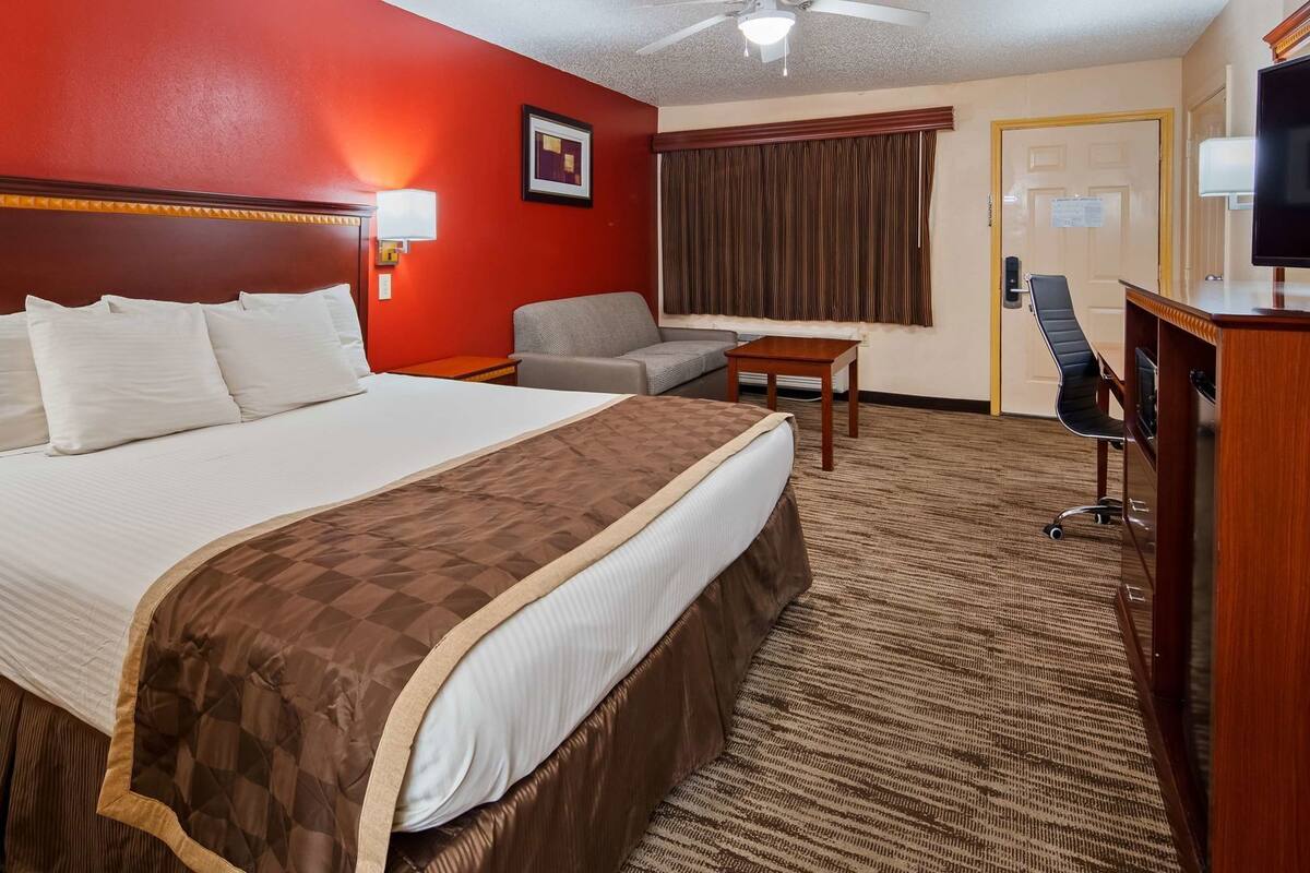 Quarto de hotel com uma cama grande, uma escrivaninha, uma cadeira, uma televisão e um ventilador de teto.