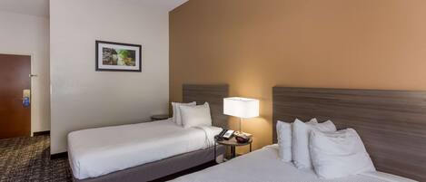 A hotel room with two beds, a nightstand with a lamp, a framed picture on the wall, and a carpeted floor.