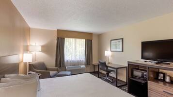 A hotel room with a bed, two chairs, a desk with a computer, a TV, and a microwave.