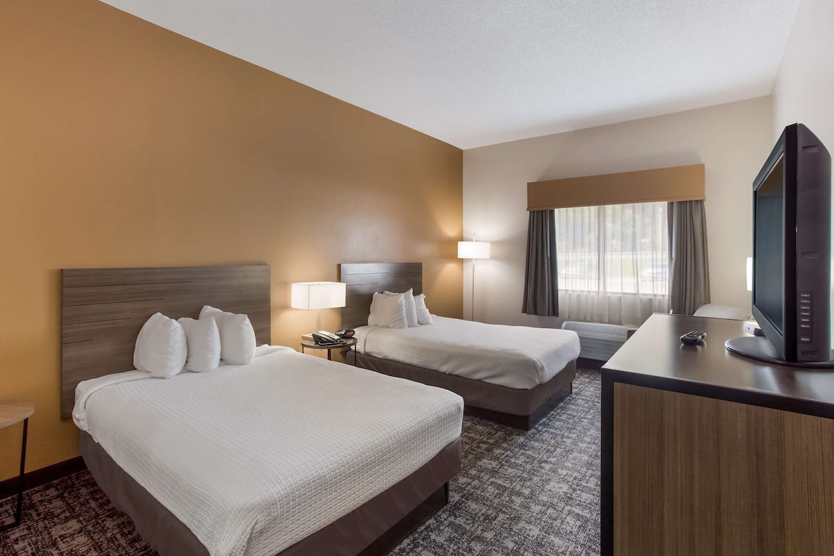 A hotel room with two beds, a desk with a television, and a lamp.