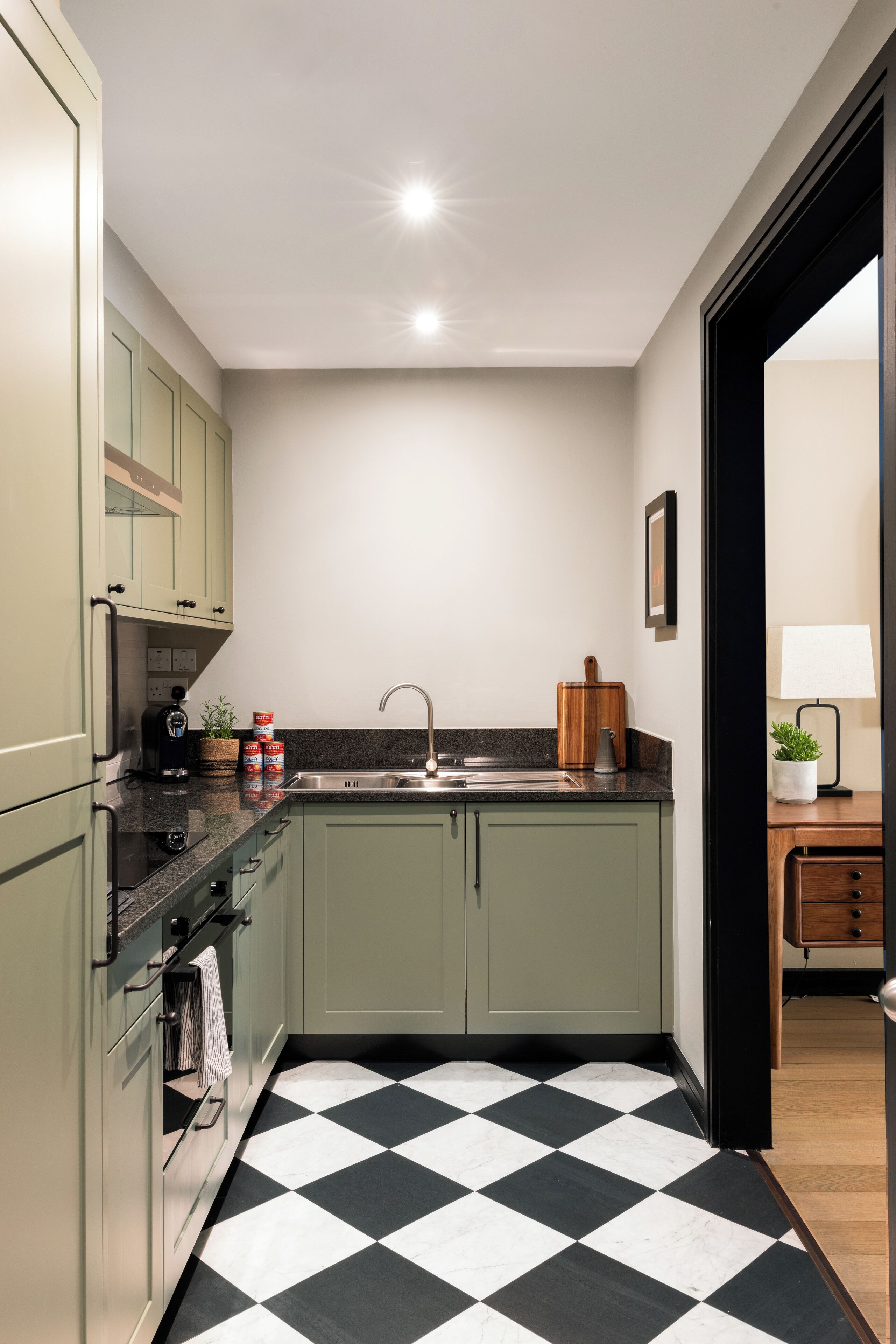 A compact kitchen with a checkered floor, a sink, and green cabinets.