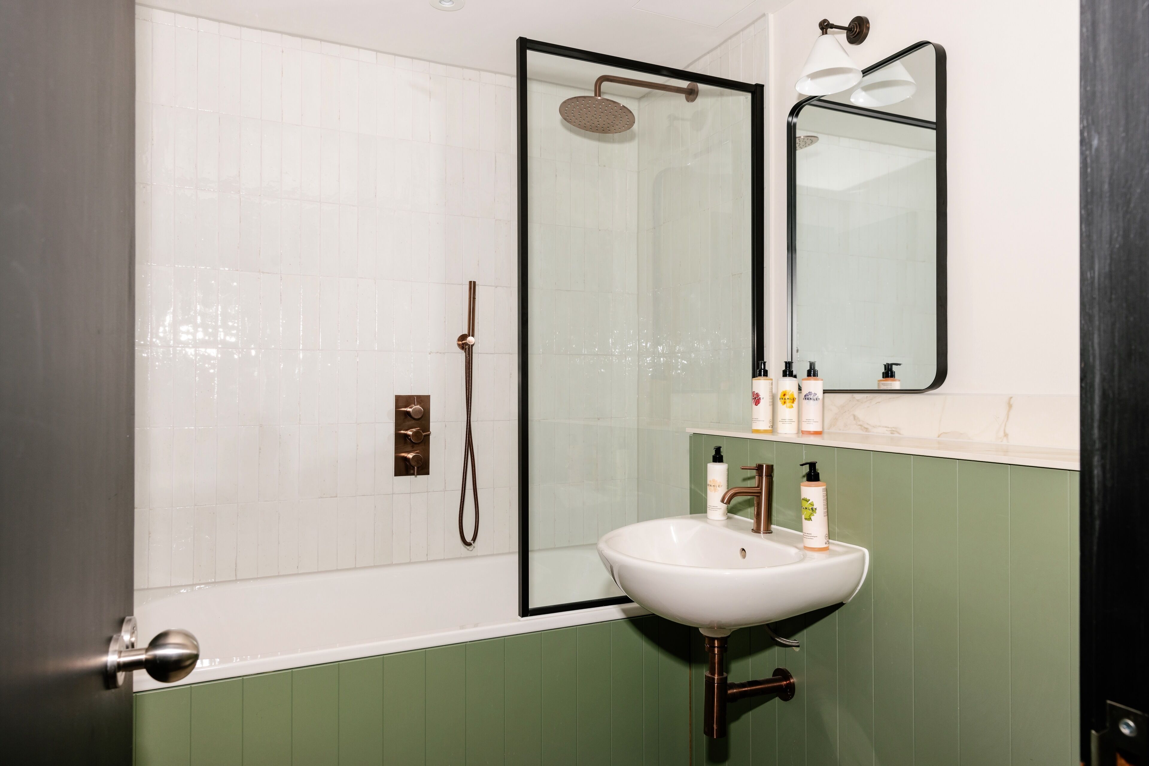 A bathroom with a white sink, green walls, a glass shower enclosure, and a mirror above the sink.