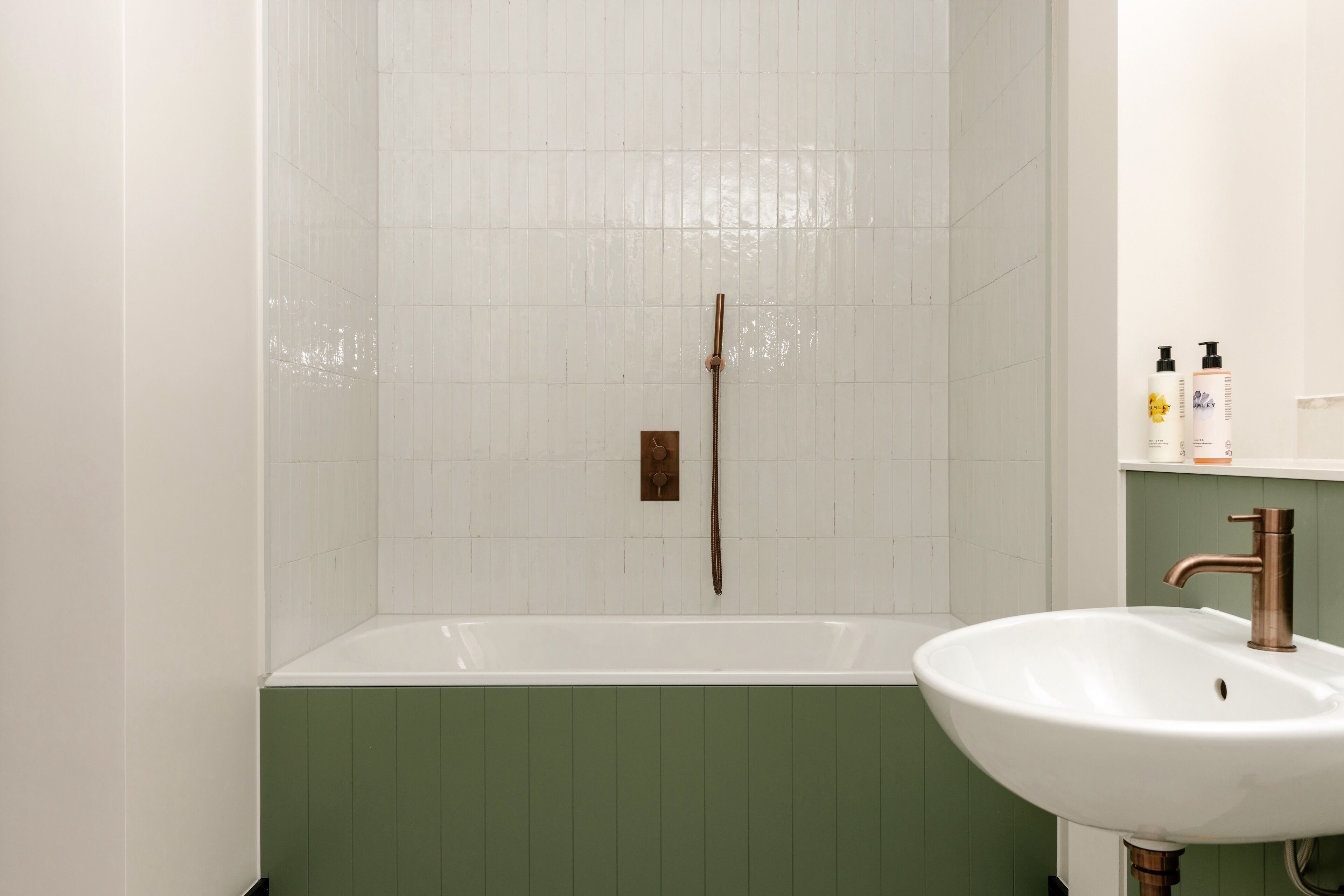 A bathroom with a white bathtub, a green vanity, and a white sink with a copper faucet.