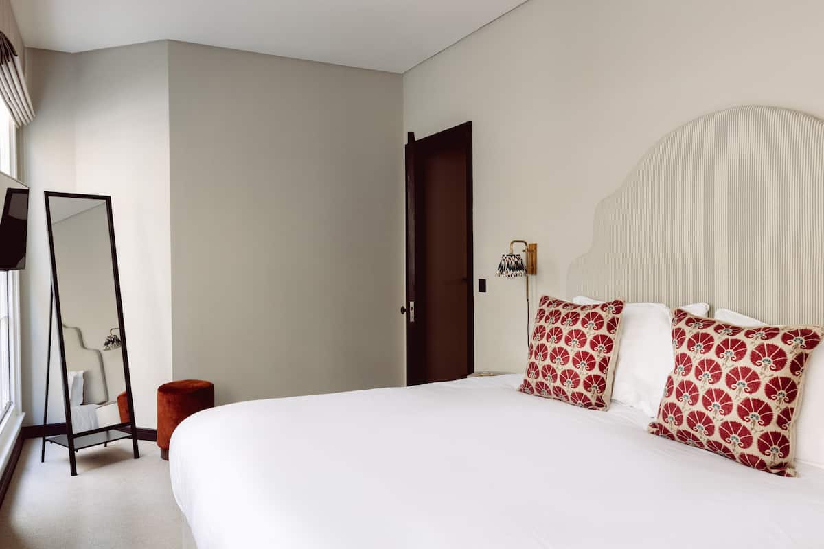 A bedroom with a large bed, a bedside table, a mirror, and a door.