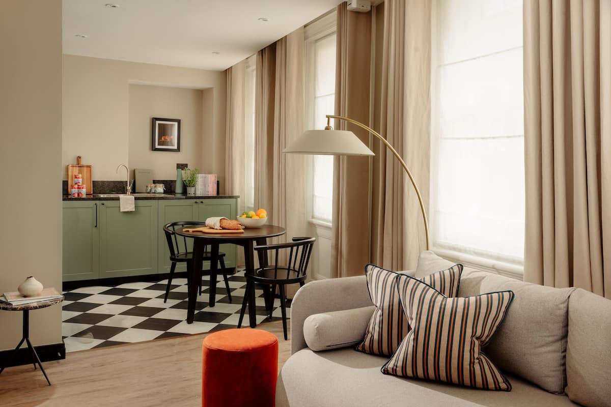 A modern living room with a sofa, striped pillows, a red ottoman, and a dining area with a table and chairs.