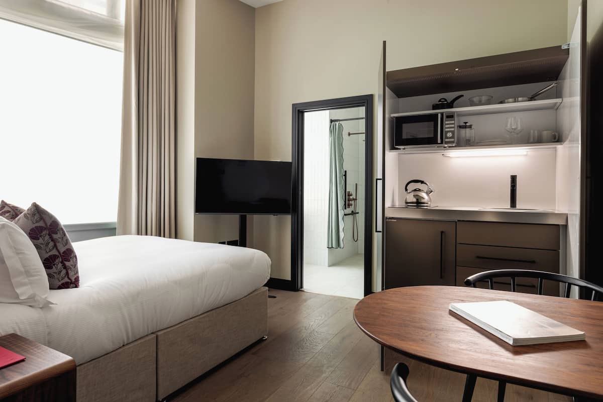 A hotel room with a bed, a TV, a dining table, and a kitchenette.