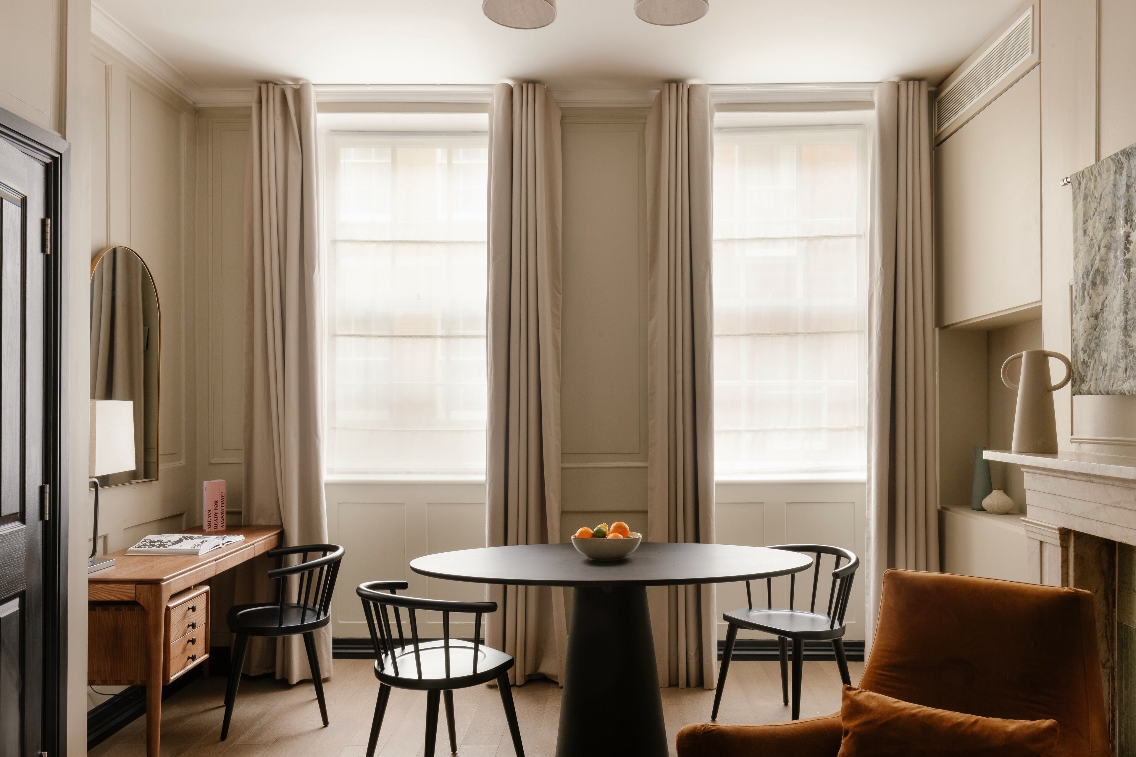 A room with a round table, four chairs, a wooden desk, and a mirror.