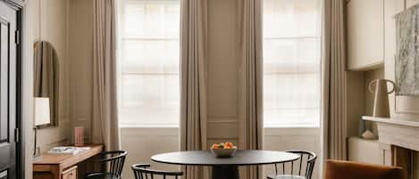 A room with a round table, four chairs, a wooden desk, and a mirror.