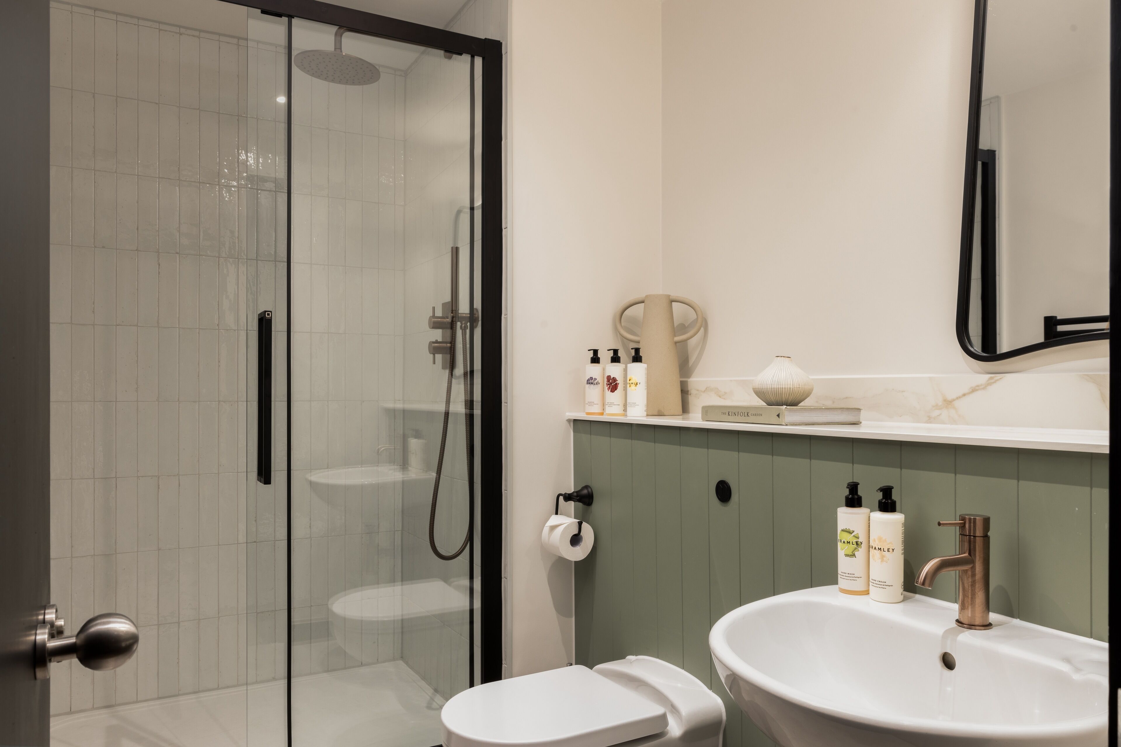 A modern bathroom with a glass shower enclosure, a white toilet, and a sink with a marble countertop.