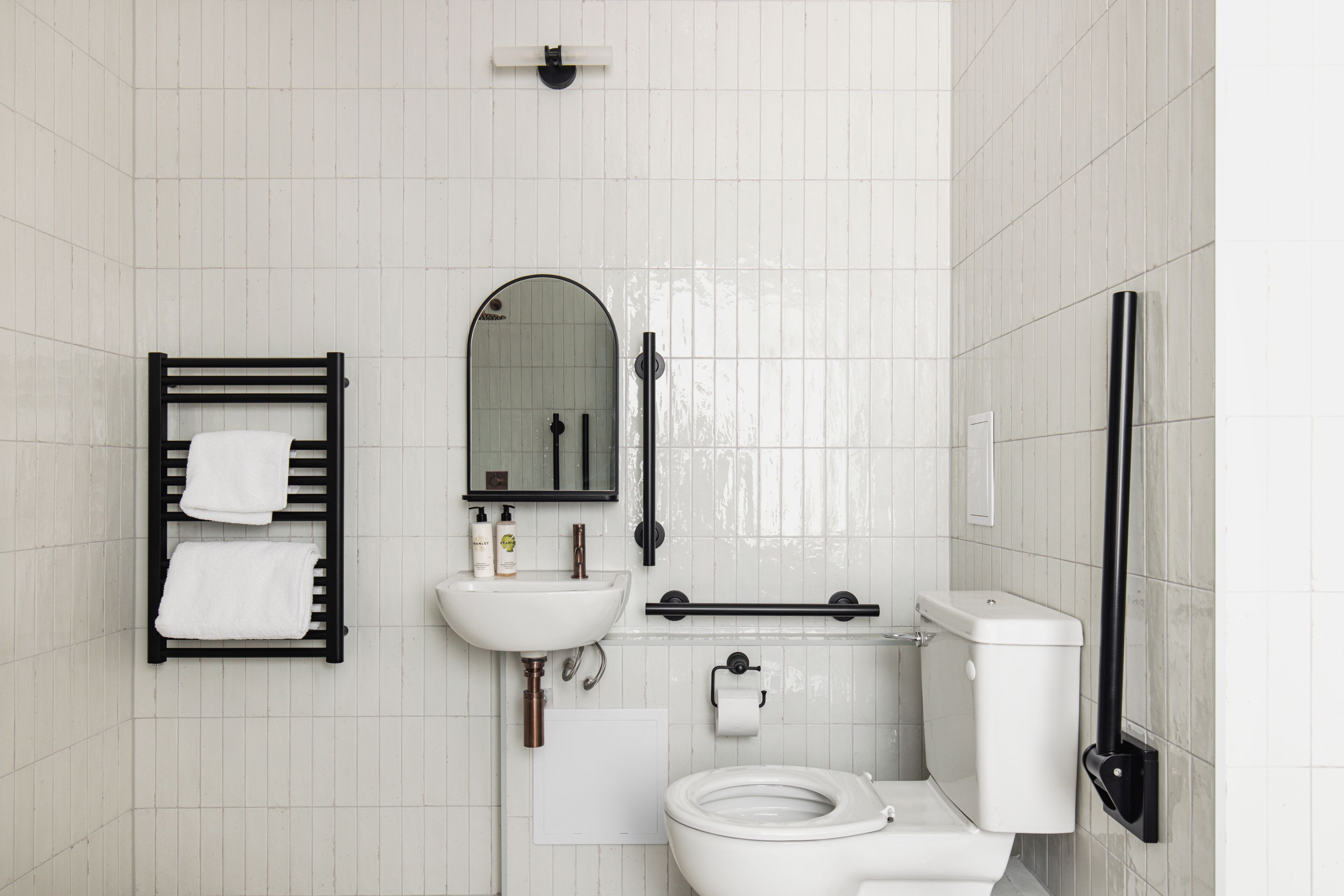 A bathroom with a toilet, sink, mirror, towel rack, and grab bars.