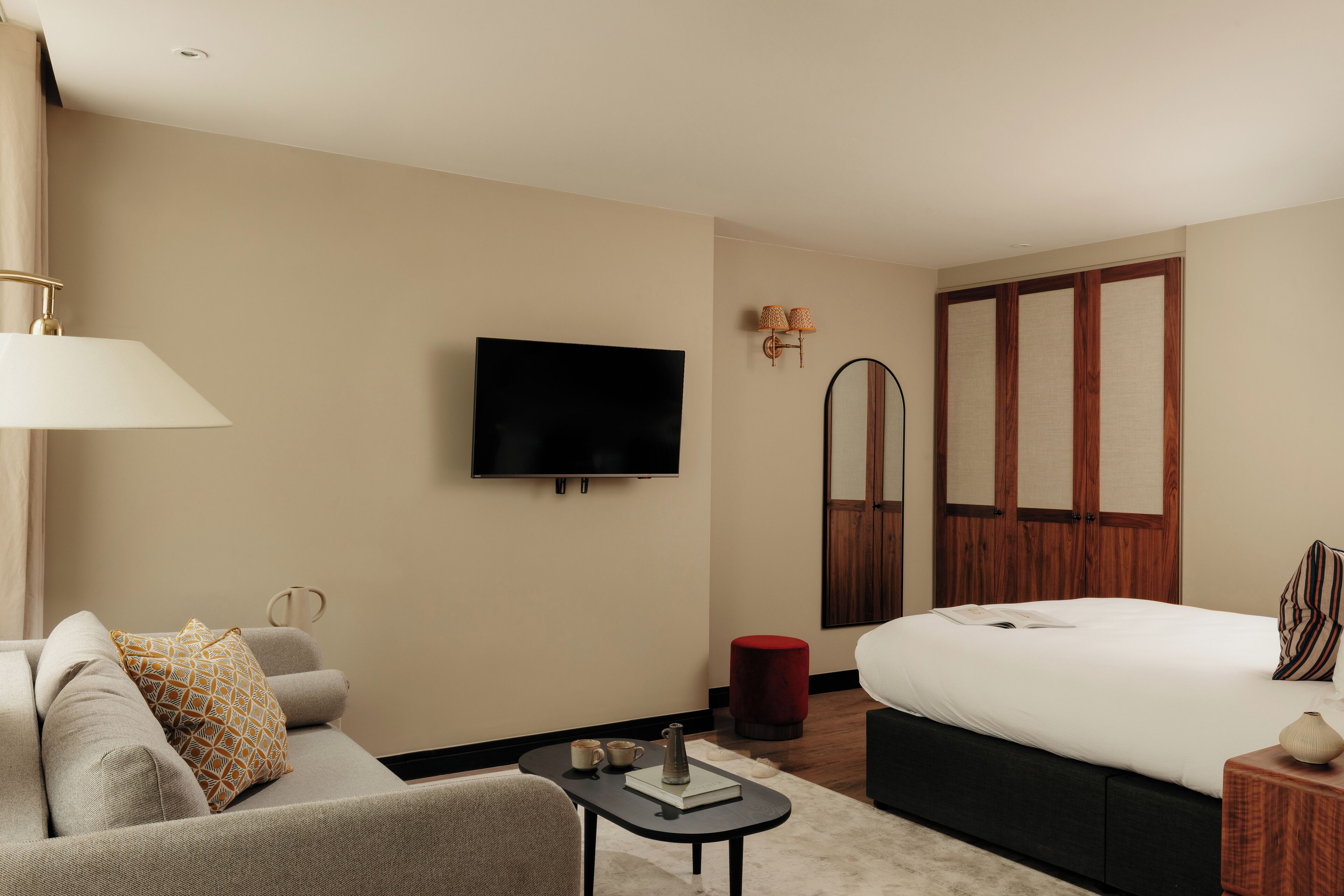A modern hotel room with a sofa, a small table, a bed, a TV, and a mirror.