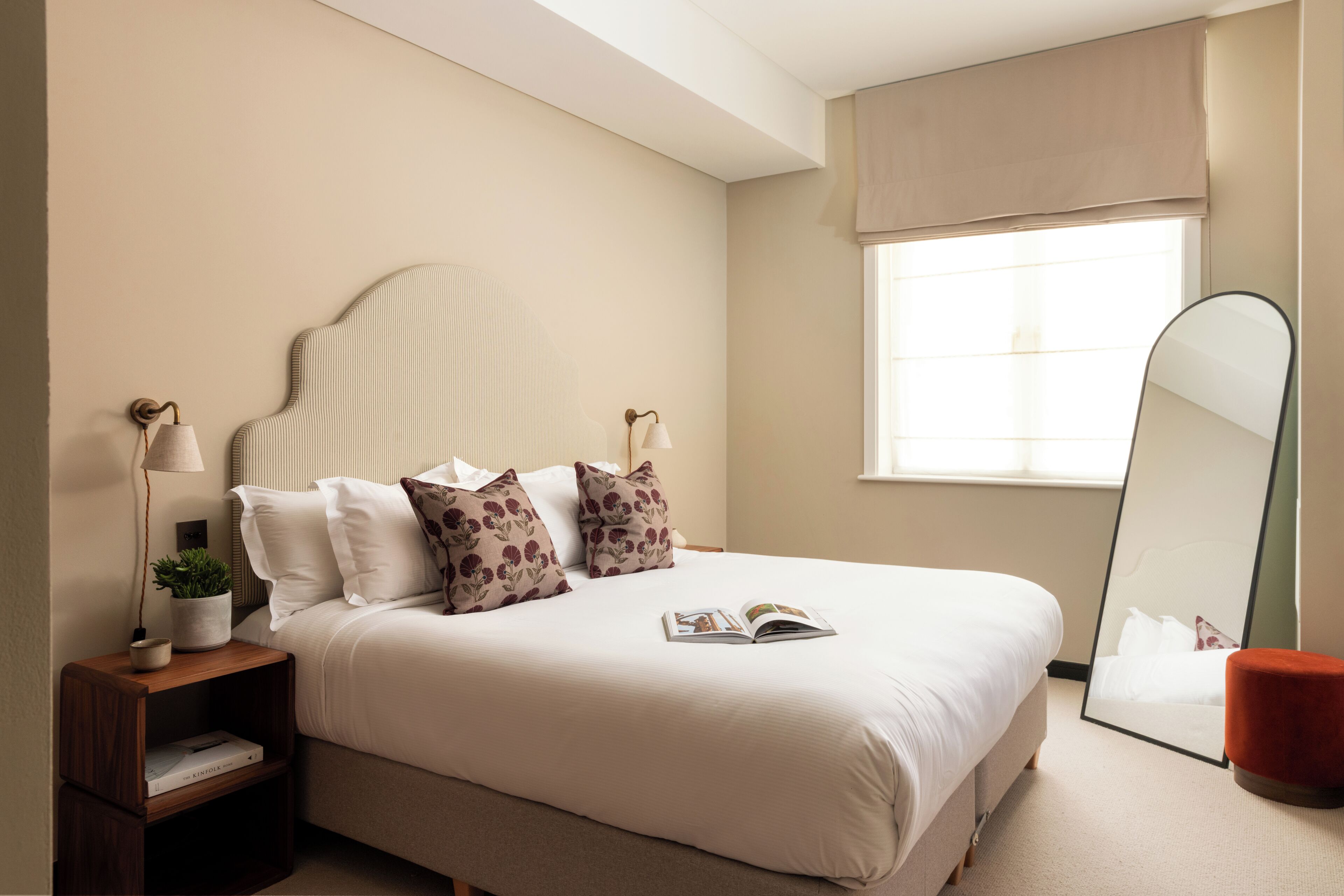 A neatly arranged bedroom with a bed, bedside table, lamp, and a large mirror.