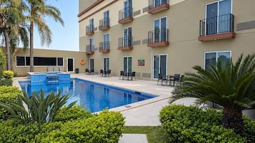Un hotel con piscina, mobiliario exterior y palmeras.