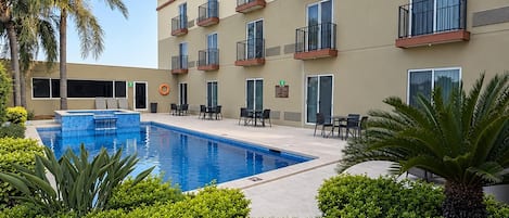 A hotel with a swimming pool, outdoor seating, and palm trees.