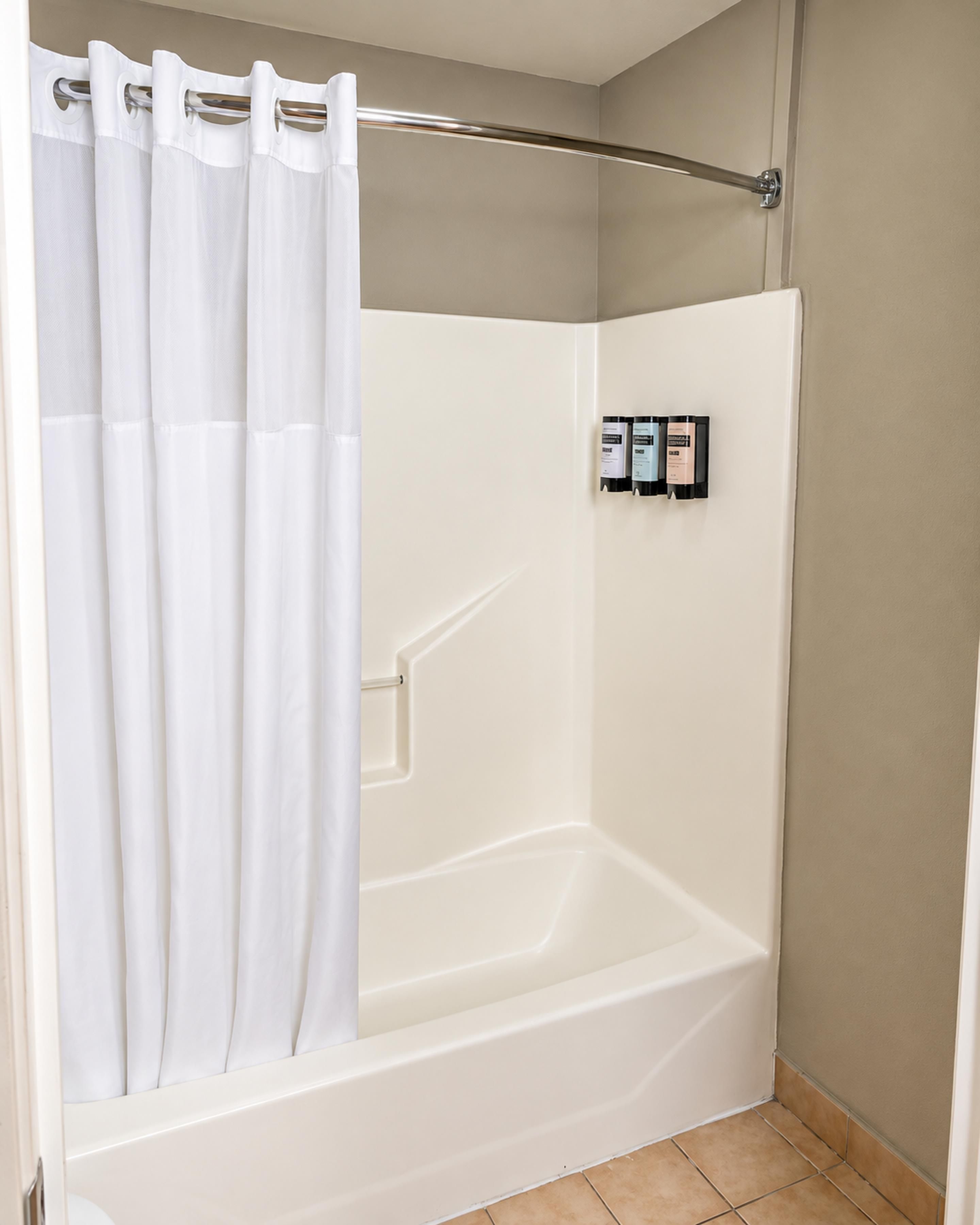 A white bathtub with a shower curtain, a towel rack, and a set of toiletries on the wall.