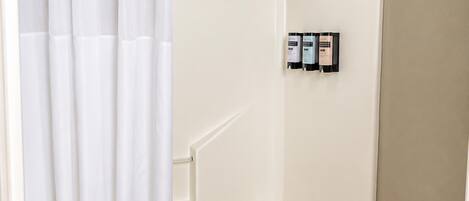 A white bathtub with a shower curtain, a towel rack, and a set of toiletries on the wall.