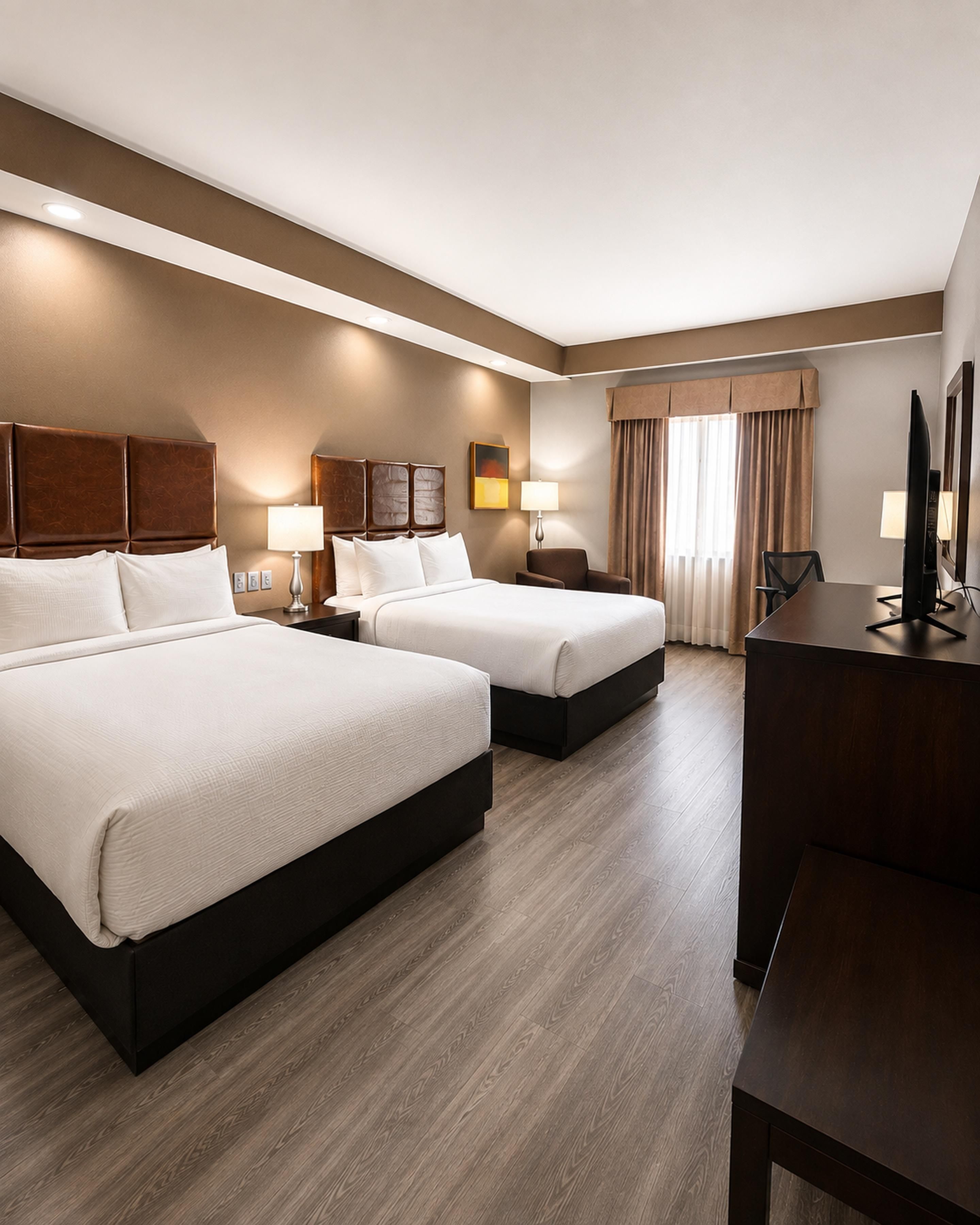 A hotel room with two beds, a desk, and a TV.
