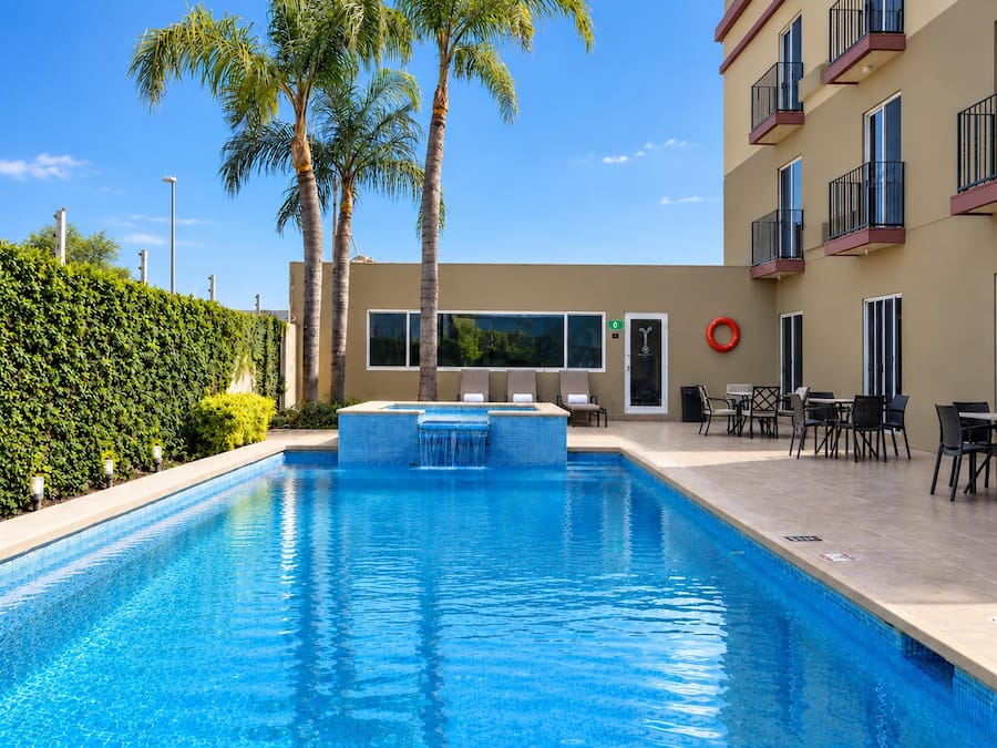 Una piscina con un jacuzzi, rodeada de palmeras y un edificio con balcones.