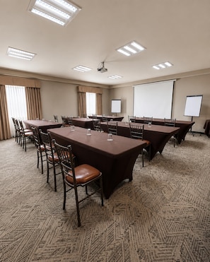 Un salón de conferencias con varias mesas y sillas, una pantalla de proyector y una pizarra.