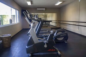 Un gimnasio con cintas de correr, un espejo grande y una ventana con vistas a zonas verdes.