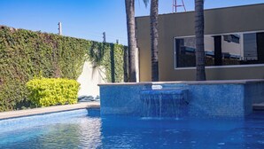 Una piscina con agua azul cristalina, rodeada de un área ajardinada con arbustos y una palmera.