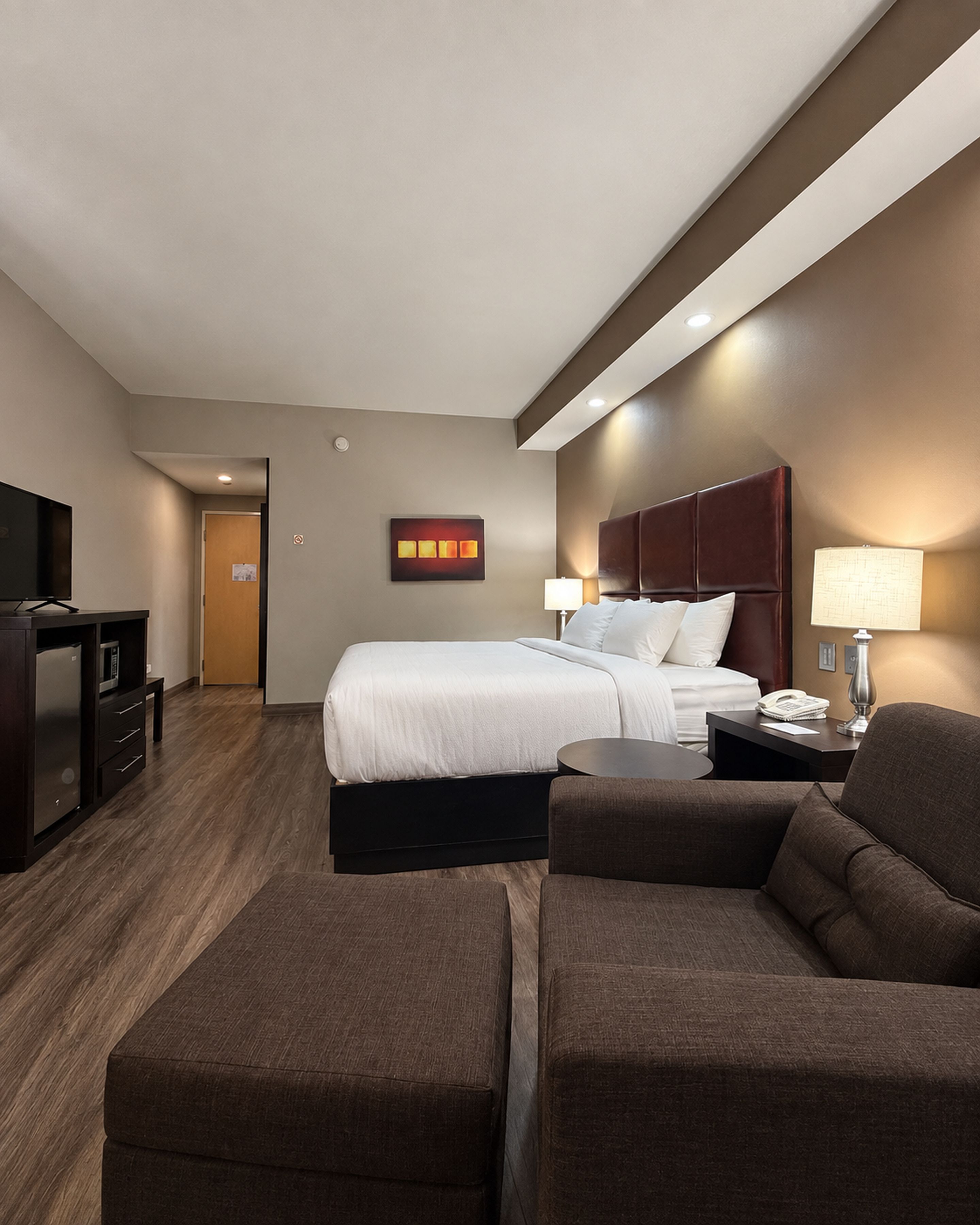 A hotel room with a bed, a desk, a chair, a TV, and a lamp.