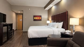 A hotel room with a bed, a desk, a chair, a TV, and a lamp.