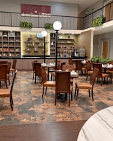 Un vestíbulo de hotel con zona de comedor, bar y escalera.
