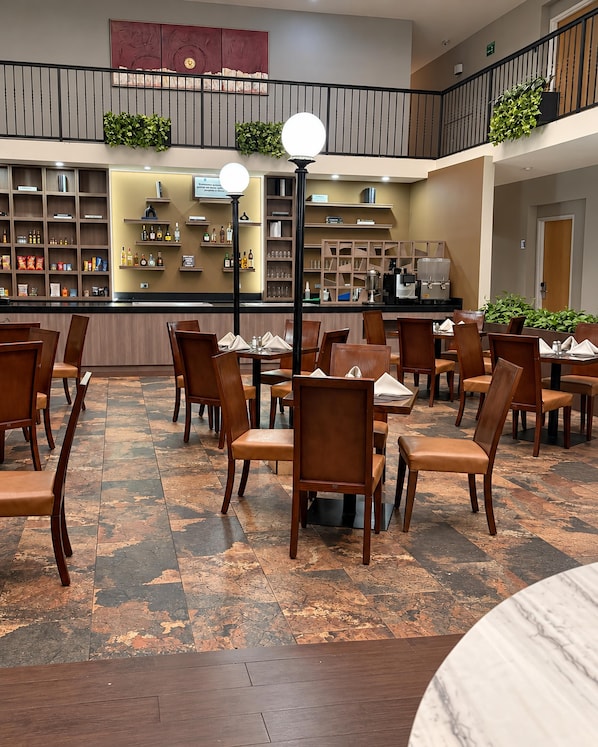 Un vestíbulo de hotel con zona de comedor, bar y escalera.