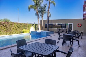 Un área junto a la piscina con un jacuzzi, mobiliario exterior y palmeras.