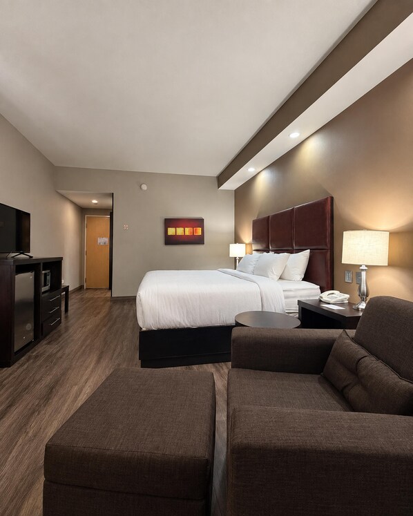 A hotel room with a bed, a desk, a TV, a lamp, and a couch.